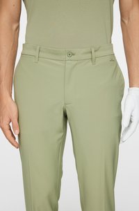 Ljusgröna byxor i ett mjukt material, med knappstängning, bälteshällor och sidofickor. Texturerad vit handske på handen.