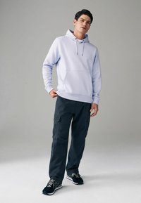 Hellblauer Hoodie mit Kängurutasche und Kordelzug, kombiniert mit dunklen Cargo-Hosen mit Seitentaschen und schwarzen sportlichen Sneakers.