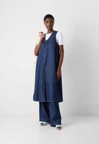 Denimkjole med ermeløst design, med knappelukking foran, sidelommer og snøring i halsen, kombinert med vide denimbukser.