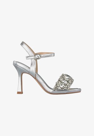 Sandali alti argentati in metallo con design open-toe, dotati di una cinghia decorativa con gemme e una fibbia su una cinghia alla caviglia regolabile.