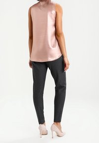 Ärmös ljusrosa satin-topp i kombination med svarta nålrandiga tapered-byxor och ljusrosa högklackade skor. Slät textur och figursydd design.