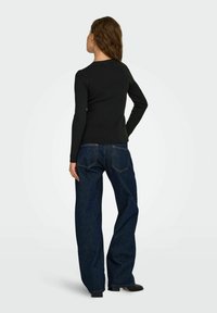 Top noir à manches longues associé à un jean en denim sombre à jambes larges. Le tissu semble lisse, et le jean présente des poches arrière et des coutures minimales.