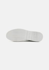 Hvit gummisåle på en sneaker med bølgete mønster og "REPLAY"-logo preget i midtseksjonen.