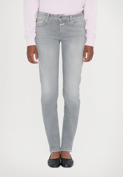 Graue Denim-Jeans mit schmaler Passform, hoher Taille, dezenter Ausbleichung und fransigem Saum. Kombiniert mit schwarzen flachen Schuhen.