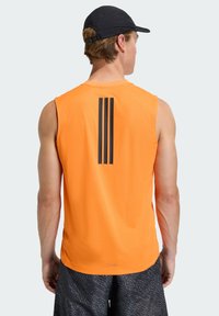 Πορτοκαλί αθλητική φανέλα χωρίς μανίκια με τρεις μαύρες κάθετες ρίγες στην πλάτη. Ομαλή υφή, σχεδιασμένη για άνεση και κινητικότητα.