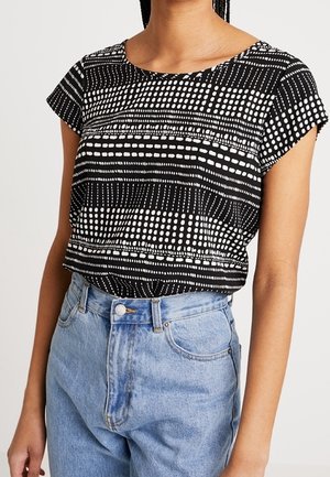 Haut noir à manches courtes avec motifs rectangulaires et ponctués blancs, porté rentré dans un jean taille haute bleu clair.
