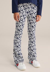 Sötétkék szellős fazonú nadrág, fehér virágos mintával, könnyű anyagból készült. Fehér sportcipővel viselve, piros és kék kiegészítőkkel.