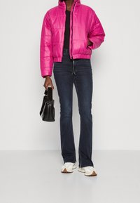 Chaqueta acolchada fucsia con cuello alto, combinada con vaqueros oscuros de campana y zapatillas cremas. Se sostiene un bolso negro estructurado en la mano.