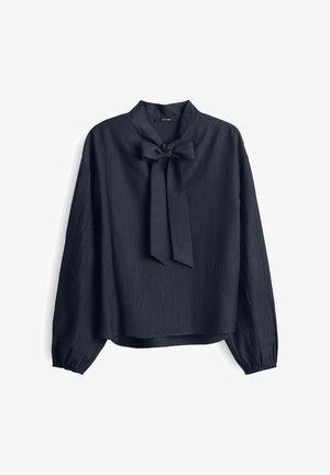 Navy blue blouse with a bow tie at the neck, long sleeves, and textured fabric. Loose fit with a rounded hem. Silky appearance.