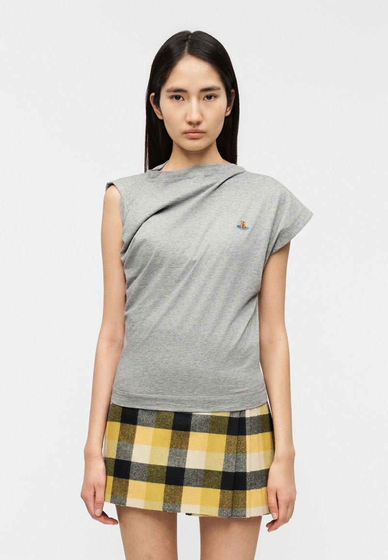 Gray short-sleeve t-shirt with draped design, featuring a small embroidered logo. Paired with a pleated yellow and black plaid skirt.