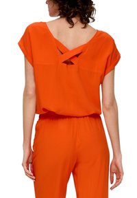 Orange jumpsuit med korte ærmer, der har en dyb V-ryg og krydset stropdetalje. Lavet af letvægts, glat stof med elastisk talje.