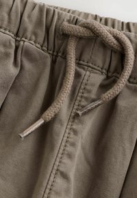 Brune bomulds shorts med elastisk talje og snørrebånd. Snørrebåndet er flettet med metalspidser. Struktureret stoffinish.