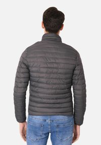 Giacca puffer grigia con colletto alto, texture trapuntata e maniche lunghe. Indossata sopra jeans di denim blu, che mettono in mostra un design slim fit.