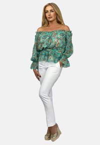 Bluzka w kolorze turkusowym, odkrywająca ramiona, z kwiatowym wzorem, z falbankami na rękawach oraz przewiązana w talii. Połączona z białymi dopasowanymi spodniami i złotymi butami na koturnie.