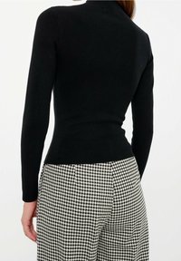 Svart randig långärmad topp med figurnära midja, kombinerad med högmidjade byxor i hundtandsmönster i svart och vitt.