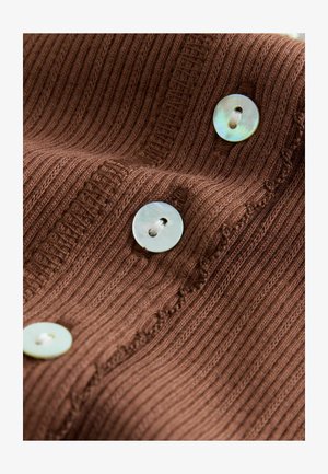 Brązowa prążkowana dzianina z poziomymi liniami, ozdobiona trzema okrągłymi, jasnymi guzikami o subtelnym połysku i centralnym otworem.