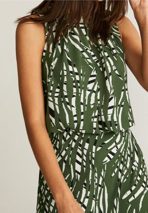 Sleeveless green top and skirt set with abstract black and white striped leaf pattern, worn by a person with medium skin tone.