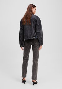 Chaqueta oversize de mezclilla negra con hombros caídos, combinada con jeans negros ajustados. Se aprecian detalles de tejido texturizado y costuras en contraste.