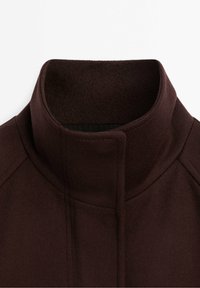 Collo in lana marrone scuro con design a collo alto e pattina dei bottoni nascosta, che mostra cuciture dettagliate e texture del tessuto.