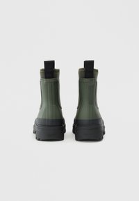 Stivali alla caviglia in gomma verde con texture rigata, suole in gomma nera e maniglia sul retro, caratterizzati da un design bicolore.