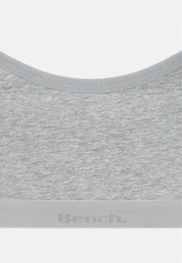Bralette in morbido tessuto grigio con scollo rotondo, cuciture lisce e una fascia con un logo in rilievo discreto nella parte inferiore.
