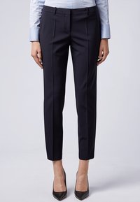 Ušité tmavě námořnické kalhoty s slim fit, jemnými předními sklady a bočními kapsami. Vyrobené z hladké tkaniny, doplněné o špičaté černé podpatky.