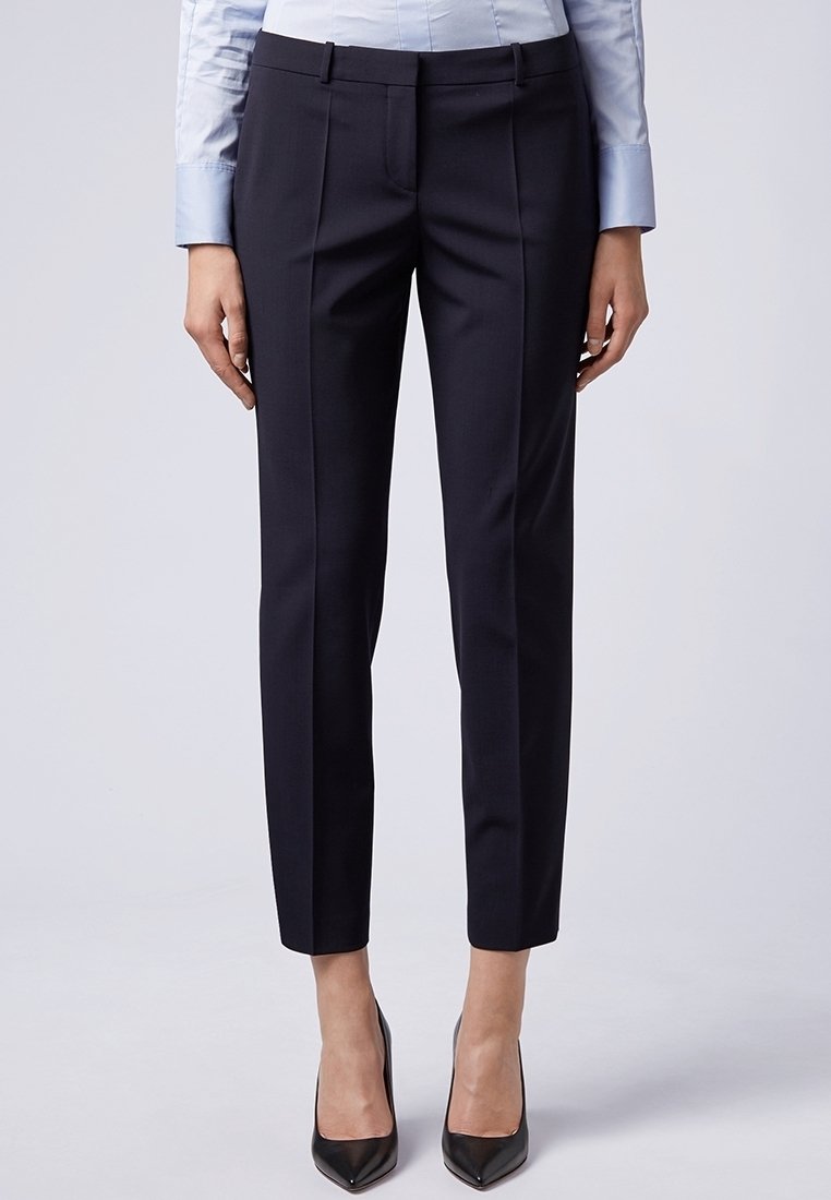 Ušité tmavě námořnické kalhoty s slim fit, jemnými předními sklady a bočními kapsami. Vyrobené z hladké tkaniny, doplněné o špičaté černé podpatky.