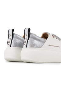 Weiße Sneaker mit strukturiertem silbernem Absatz, Schnürdesign, schwarzen Akzenten und einer dicken weißen Sohle. Mit Markenlogos auf der Rückseite und der Zunge.