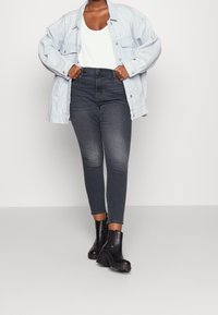 Ljusblå denim oversized jacka, vit linne, mörka slim-fit jeans och svarta ankelstövlar med klumpig klack och dragkedjedetalj.