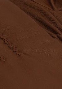 Bruine leren textuur met zichtbare stiknaden, met een glad, licht gerimpeld oppervlak. Materiaal lijkt zacht en soepel.