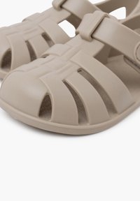 Sandalias de plástico moldeado beige con diseño de punta abierta, que cuentan con correas horizontales y verticales para la ventilación y la comodidad.