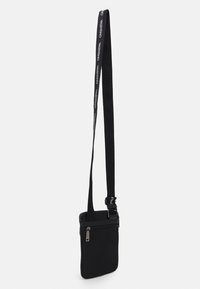 Geantă crossbody neagră cu textură netedă, curea ajustabilă cu logo, închidere cu fermoar și design plat pentru transport ușor.