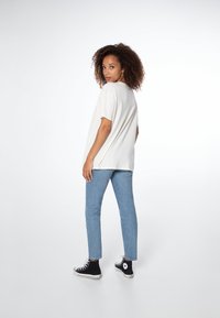 Lichtbeige oversized t-shirt met korte mouwen, gecombineerd met lichtblauwe slim fit jeans en zwarte high-top sneakers. Eenvoudig ontwerp, ontspannen pasvorm.