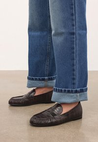 Pruunid nahast loafers, millel on tekstuuriga viimistlus, ümar varvas ja elastsed küljed, sobitatud pahkluude juures üles keeratud teksapükstega.