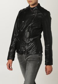 Svart lädermotorcykeljacka med dubbelknäppning, dragkedjefickor och strukturerade axlar. Figursydd design med krage.