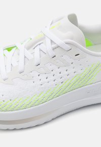 Scarpa sportiva bianca con dettagli in verde neon. Caratterizzata da una parte superiore in tessuto traspirante, chiusura con lacci e una suola leggera e testurizzata.