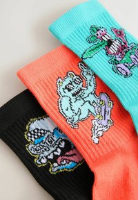 Tres pares de calcetines de punto: uno negro, uno coral y uno turquesa, cada uno con diseños de animales en un estilo caricaturesco y colores vibrantes.