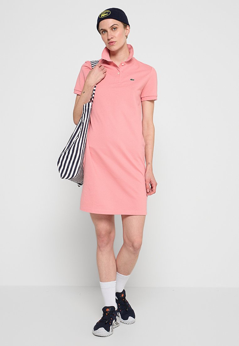Robe polo rose en coton, avec un col, des manches courtes et un logo sur la poitrine. Assortie à un sac fourre-tout rayé.