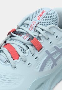 Ανοιχτό μπλε αθλητικό παπούτσι με επάνω μέρος από διχτυωτό ύφασμα, γκρίζο λογότυπο και κόκκινες λεπτομέρειες. Περιλαμβάνει υφές με επικάλυψη και παραδοσιακό σύστημα κορδονιών.