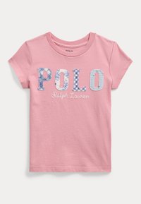 Vaaleanpunainen lyhythihainen t-paita, jossa on 'POLO' monivärisillä kukka- ja ruutukuvioilla, ja alla kirjailtu 'Ralph Lauren'.