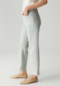 Jeans in denim verde chiaro con vestibilità a gamba dritta, vita media, tasche frontali e dettagli di cucitura discreti. Indossati con scarpe ballerina nude.