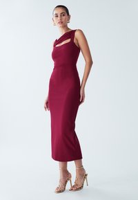 Vyno raudonumo, kūną apgaubiančios suknelės su iškirpte ir asimetriškomis petnešėlėmis. Lygi tekstūra ir vidutinio ilgio iki blauzdos. Derinama su dirželiais apkabinančiomis aukštakulnėmis.