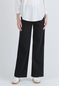 Černé široké kalhoty s vysokým pasem vyrobené z měkké bavlněné směsi, v kombinaci s bílými teniskami pro neformální vzhled.