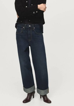 Dark blue denim jeans with a relaxed fit, featuring rolled cuffs and classic five-pocket design. Material is thick and sturdy, with subtle stitching details.