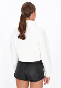 Kort hvid bomuldspullover med høj krave, kombineret med sorte letvægts-shorts. Har ribbede ærmegab og elastisk taljebånd.