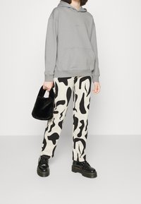 Felpa grigia, pantaloni crema con motivi astratti neri, borsa nera in pelliccia sintetica e stivali neri con lacci e suola chunky.