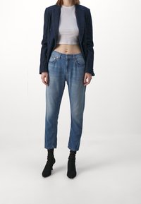 Vaqueros de mezclilla azul claro con un corte relajado, acabado desteñido, cinco bolsillos y costuras en contraste, combinados con una camiseta gris recortada y botines negros.