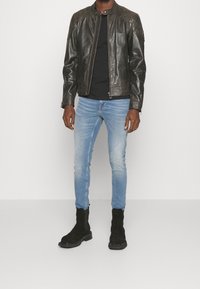 Svart läderjacka med ståkrage, kombinerad med ljusblå smala jeans och svarta mockastövlar. Slät yta, figursydd design.