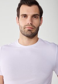Biała koszulka typu crewneck wykonana z gładkiego materiału, z krótkimi rękawami i dopasowanym krojem, z minimalnie widocznym logo lub wzorami.
