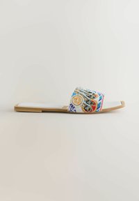 Sandale plate avec semelle beige et dessus de pied rembourré blanc, dotée d'une large bride décorée de perles multicolores et de motifs géométriques.